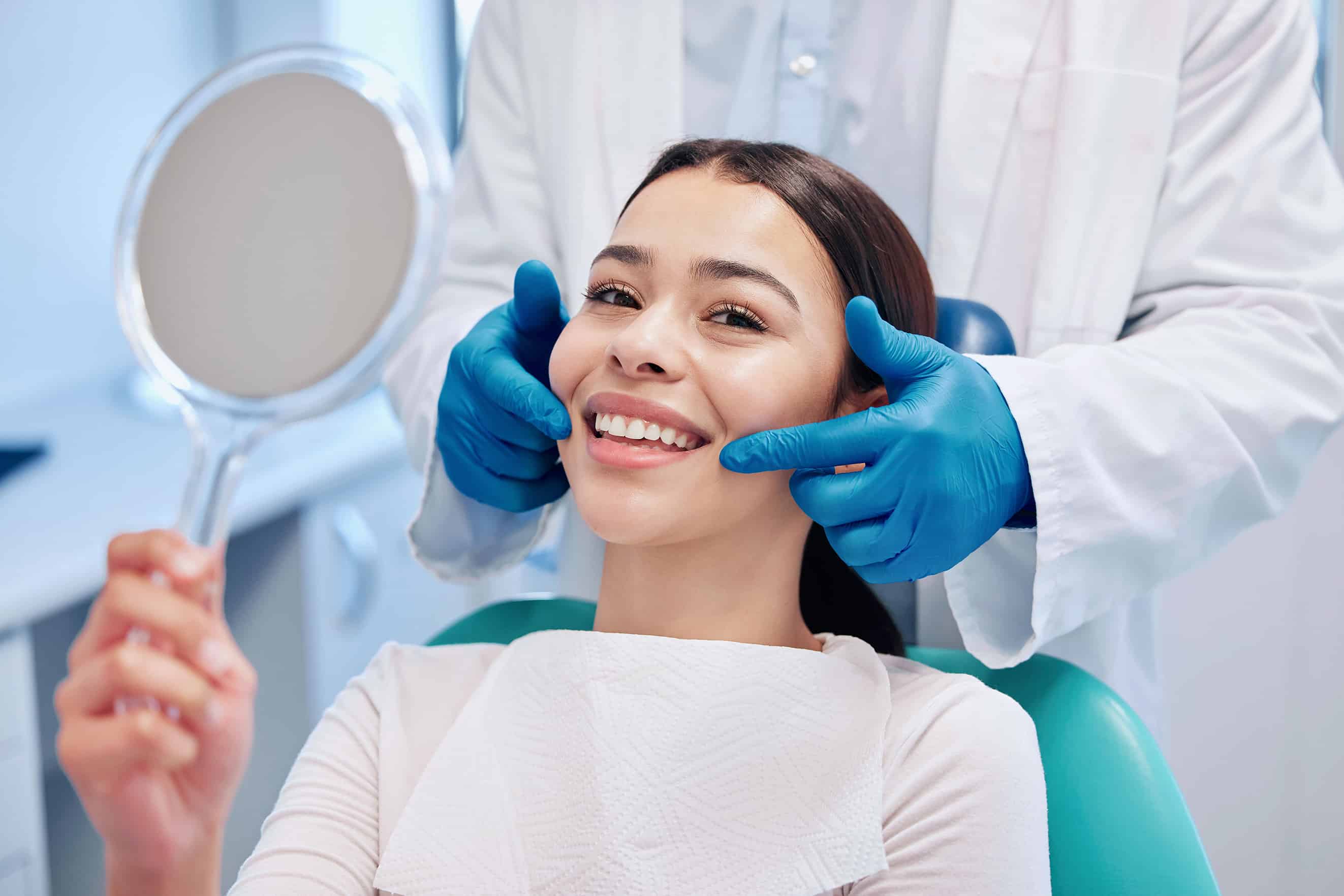 woman smiling with mirror at dental appt - Nouvelle Dentistry